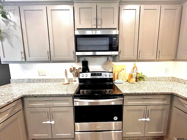 kitchen with stainless steel appliances, light stone countertops, and gray cabinetry