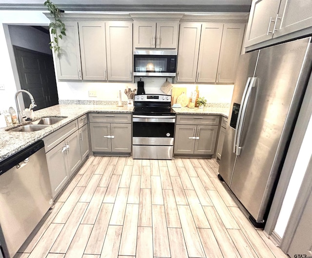 kitchen with sink, gray cabinets, kitchen peninsula, stainless steel appliances, and light stone countertops