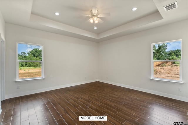 unfurnished room with ceiling fan, a raised ceiling, dark hardwood / wood-style floors, and plenty of natural light