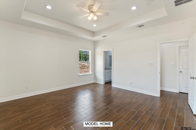 spare room with dark wood-type flooring, ceiling fan, and a raised ceiling