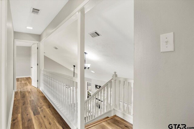 corridor with a chandelier, hardwood / wood-style floors, and vaulted ceiling