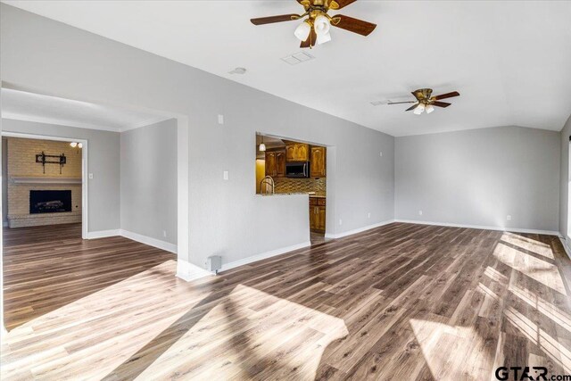 unfurnished living room featuring hardwood / wood-style flooring, ceiling fan, lofted ceiling, and a fireplace