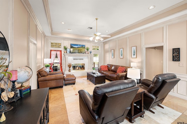 living room with a decorative wall, a glass covered fireplace, visible vents, ornamental molding, and a raised ceiling