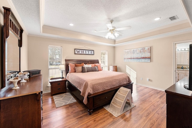 bedroom featuring baseboards, visible vents, a raised ceiling, wood finished floors, and crown molding