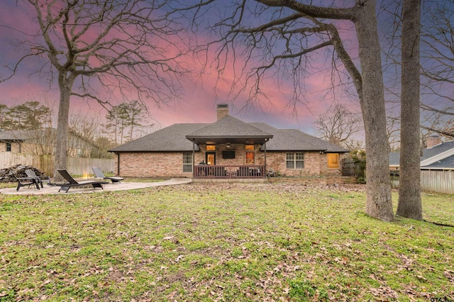 view of front of home featuring brick siding, fence, a yard, a chimney, and a patio area