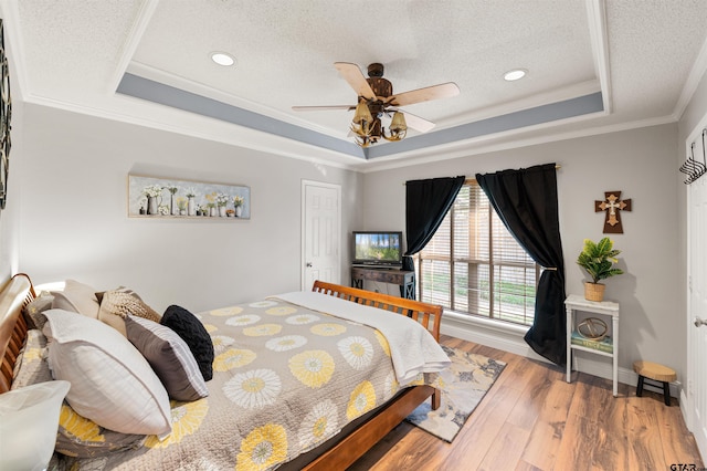 bedroom with light wood-style floors, a raised ceiling, and a textured ceiling