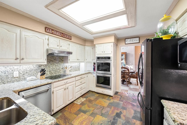 kitchen with appliances with stainless steel finishes, light stone countertops, stone finish flooring, under cabinet range hood, and backsplash