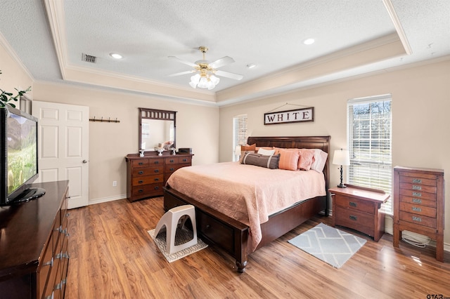 bedroom featuring a textured ceiling, wood finished floors, visible vents, ornamental molding, and a raised ceiling