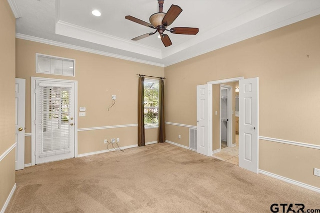carpeted spare room with crown molding, a wealth of natural light, a ceiling fan, and a tray ceiling