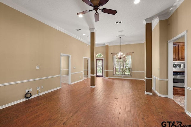 unfurnished living room with crown molding, ceiling fan with notable chandelier, baseboards, visible vents, and decorative columns