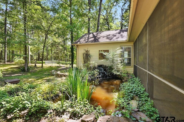 view of home's exterior featuring a shingled roof and a small pond