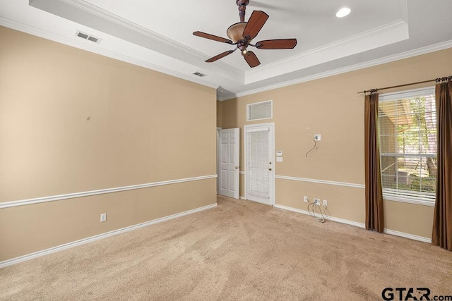 carpeted spare room with a tray ceiling, visible vents, and ornamental molding