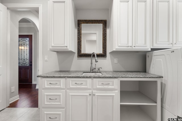 kitchen with washer / clothes dryer, white cabinets, arched walkways, a sink, and light stone counters