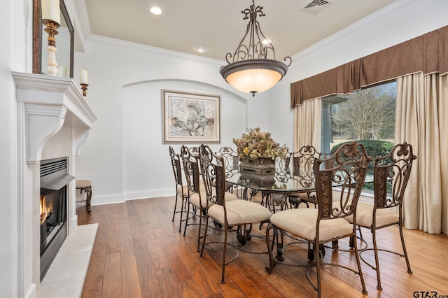 dining area featuring hardwood / wood-style flooring, crown molding, and a tile fireplace