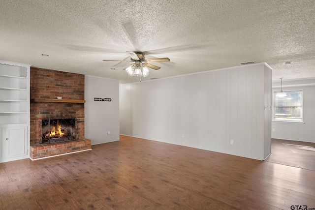 unfurnished living room featuring a brick fireplace, a textured ceiling, ceiling fan, wooden walls, and hardwood / wood-style floors