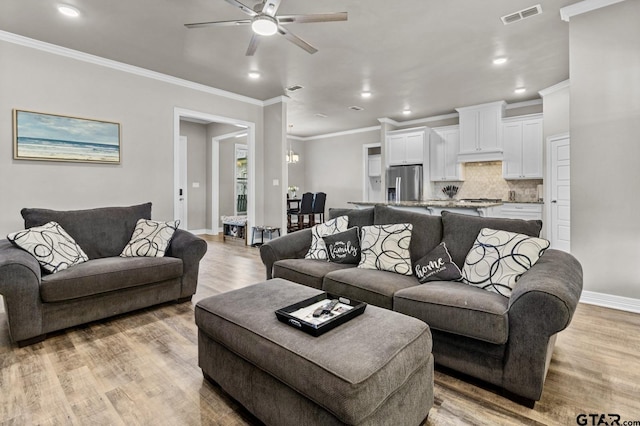 living area featuring light wood finished floors, baseboards, visible vents, ceiling fan, and ornamental molding