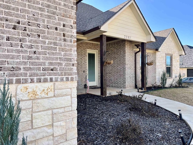 view of exterior entry featuring brick siding and a shingled roof