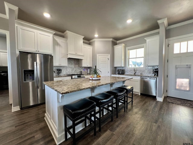 kitchen with appliances with stainless steel finishes, a center island, light stone countertops, white cabinetry, and a sink