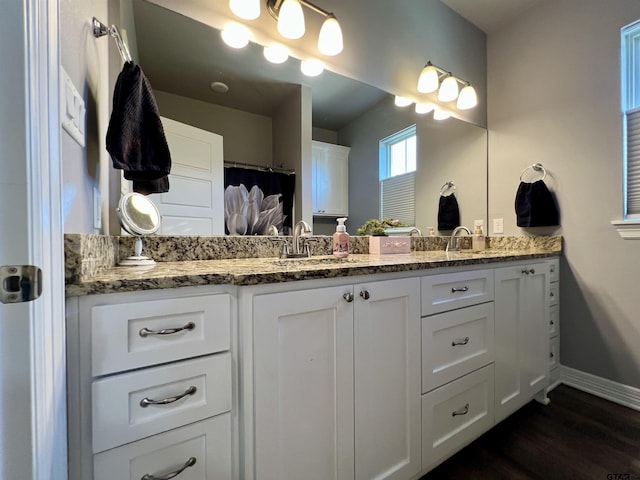 full bath featuring double vanity, baseboards, a sink, and wood finished floors