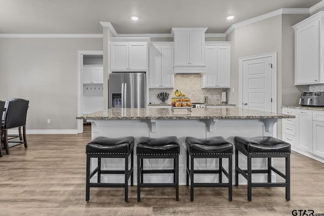 kitchen featuring stainless steel refrigerator with ice dispenser, a breakfast bar area, a center island with sink, and white cabinets