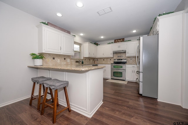 kitchen with a kitchen bar, white cabinetry, appliances with stainless steel finishes, dark hardwood / wood-style floors, and kitchen peninsula