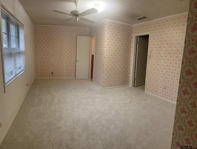 empty room featuring a textured ceiling, ceiling fan, crown molding, and light carpet