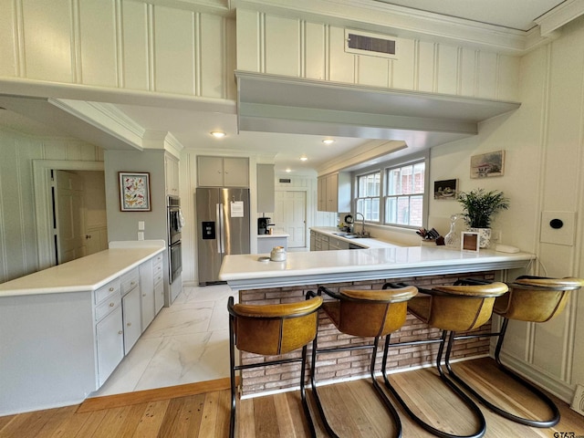 kitchen featuring stainless steel appliances, a kitchen breakfast bar, light hardwood / wood-style flooring, and crown molding