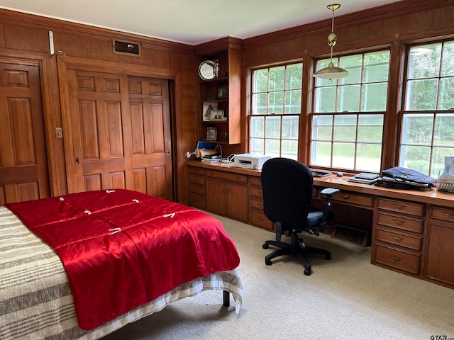 bedroom featuring built in desk, wooden walls, light colored carpet, and crown molding