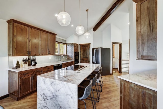 kitchen with light stone countertops, backsplash, black appliances, pendant lighting, and a center island