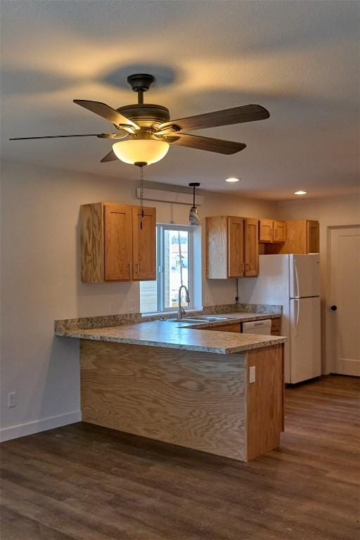 kitchen featuring a peninsula, a sink, freestanding refrigerator, dark wood-style floors, and brown cabinetry