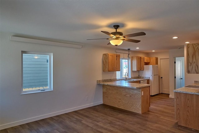 kitchen with dark wood-style flooring, freestanding refrigerator, a sink, a peninsula, and baseboards