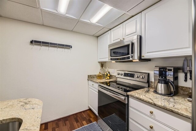 kitchen featuring white cabinetry, a drop ceiling, light stone countertops, dark hardwood / wood-style flooring, and appliances with stainless steel finishes