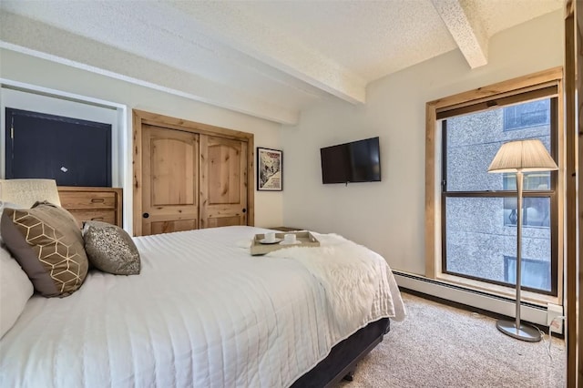 bedroom with carpet, baseboard heating, a textured ceiling, beamed ceiling, and a closet