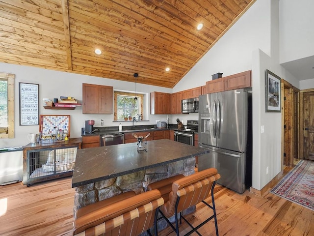 kitchen featuring a breakfast bar area, high vaulted ceiling, hanging light fixtures, a kitchen island, and appliances with stainless steel finishes