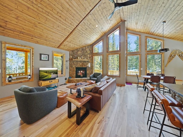 living room with light wood-type flooring, ceiling fan, high vaulted ceiling, wood ceiling, and a stone fireplace