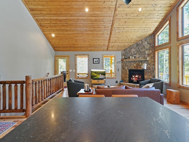 living room featuring wooden ceiling, vaulted ceiling, light wood-type flooring, plenty of natural light, and a stone fireplace