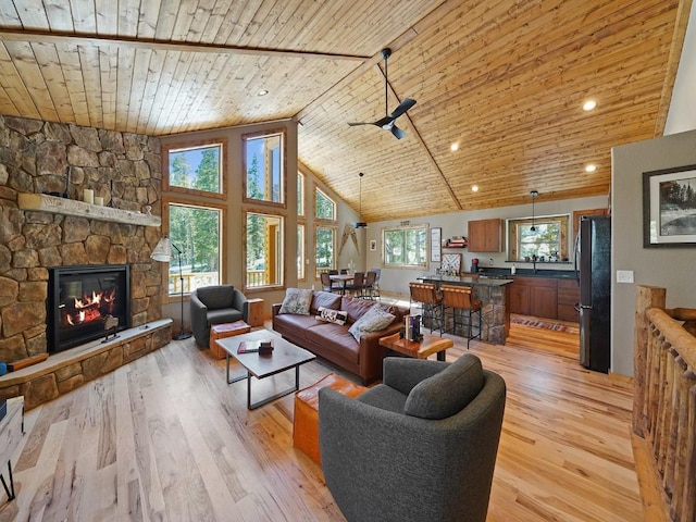 living room featuring wood ceiling, light hardwood / wood-style flooring, a stone fireplace, and high vaulted ceiling