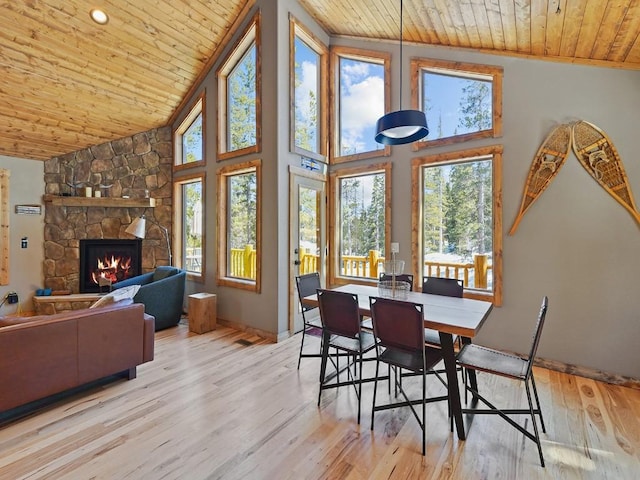 dining room with wooden ceiling, a healthy amount of sunlight, high vaulted ceiling, a fireplace, and light hardwood / wood-style flooring