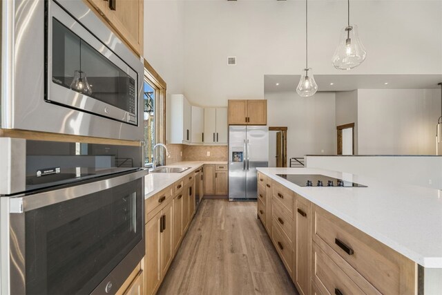 kitchen with sink, hanging light fixtures, stainless steel appliances, light hardwood / wood-style flooring, and backsplash