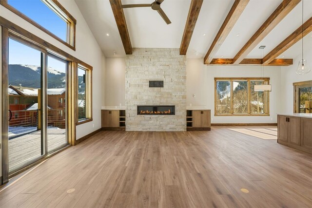 unfurnished living room featuring light wood-type flooring, ceiling fan, beamed ceiling, a mountain view, and a stone fireplace