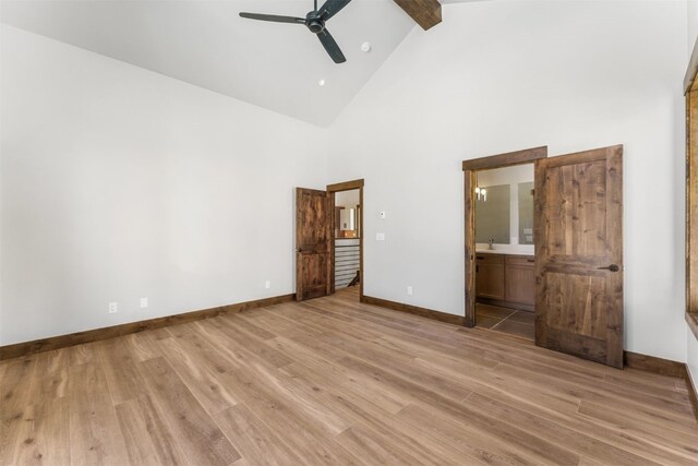 unfurnished bedroom featuring beam ceiling, connected bathroom, ceiling fan, light hardwood / wood-style flooring, and high vaulted ceiling