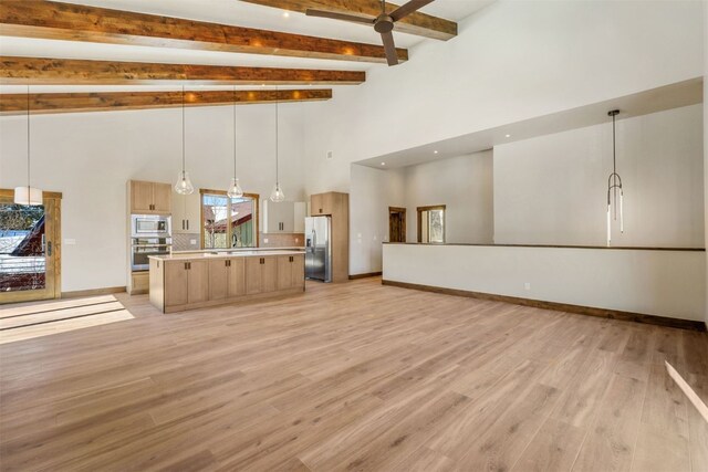 unfurnished living room featuring ceiling fan, sink, a high ceiling, light hardwood / wood-style flooring, and beamed ceiling