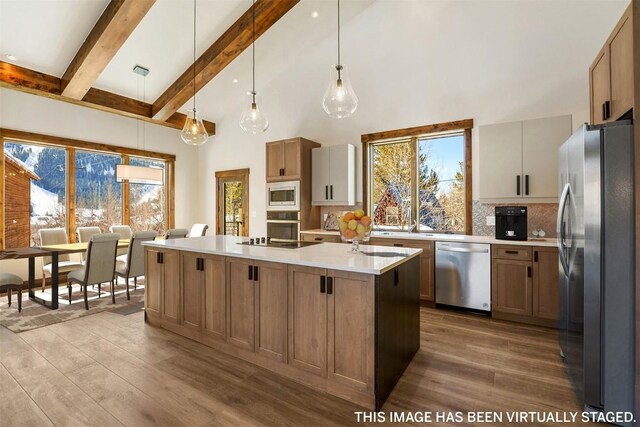 kitchen with light hardwood / wood-style flooring, backsplash, pendant lighting, a kitchen island with sink, and appliances with stainless steel finishes