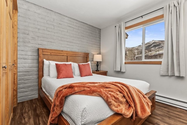 bedroom with a mountain view, dark wood-type flooring, a baseboard radiator, and brick wall