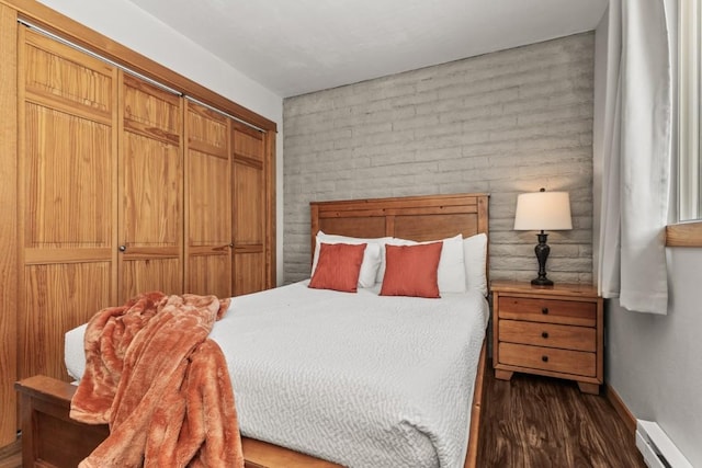 bedroom with brick wall, a baseboard heating unit, dark hardwood / wood-style floors, and a closet