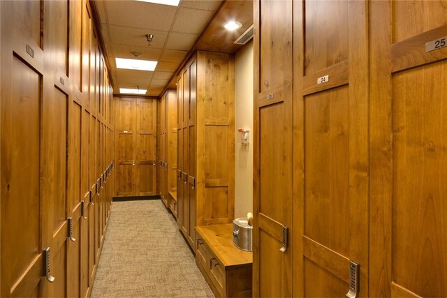 hall with wooden walls, a drop ceiling, and light colored carpet