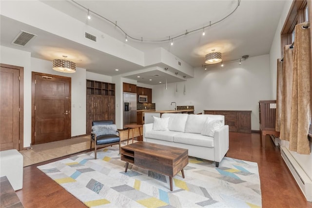 living area with a baseboard radiator, visible vents, and track lighting