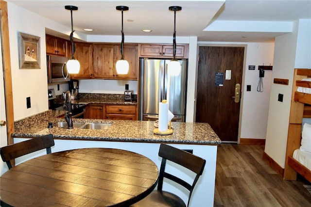 kitchen featuring kitchen peninsula, dark stone counters, stainless steel appliances, dark wood-type flooring, and pendant lighting