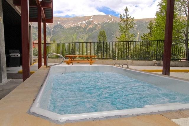 view of swimming pool with a grill, a mountain view, and a hot tub