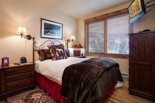 bedroom featuring light wood-type flooring and a baseboard heating unit